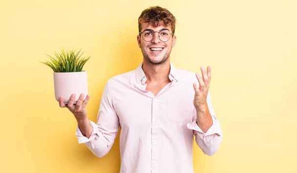 young handsome man feeling happy, surprised realizing a solution or idea. decorative plant concept - Foto, Imagem