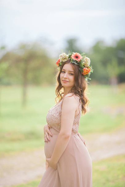 Portrait of a young pregnant woman with a wreath on her head in the park. Pregnancy. - Photo, Image