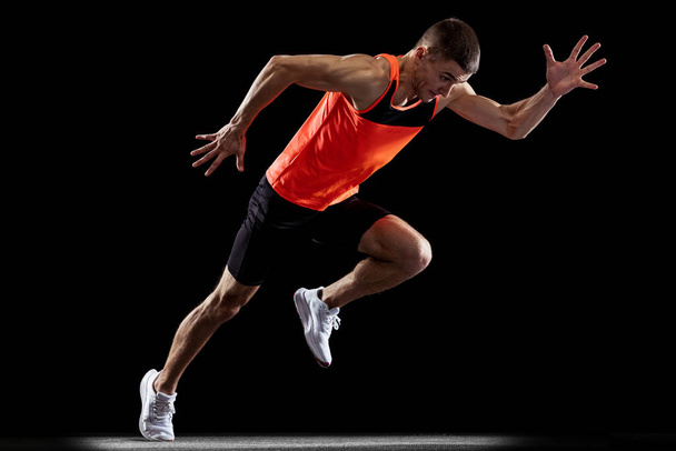 Full-length back view portrait of young male professional athlete running, training isolated over black studio background - Photo, image