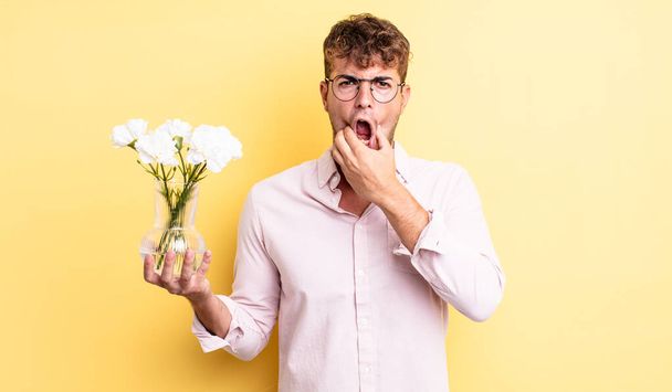 young handsome man with mouth and eyes wide open and hand on chin. flowers concept - Zdjęcie, obraz