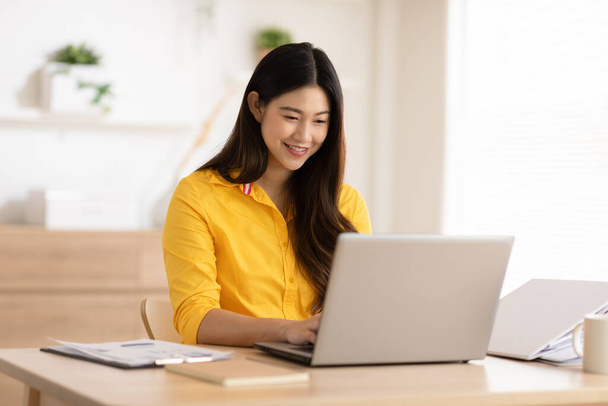 Entrepreneur beautiful business asian young woman wear yellow shirt work online with laptop at home.Freelance woman working online sale marketing at home.Small Business Startup concept.Tracking Shot - Фото, зображення