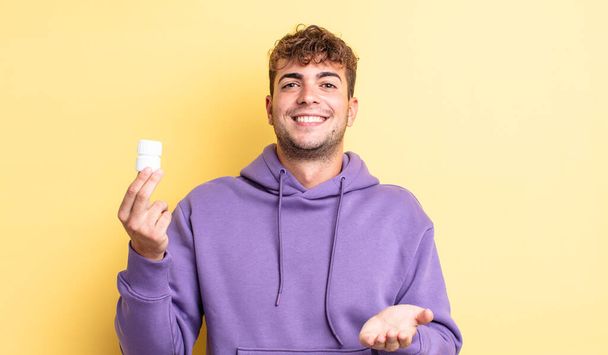 young handsome man smiling happily with friendly and  offering and showing a concept. pills bottle concept - Photo, image
