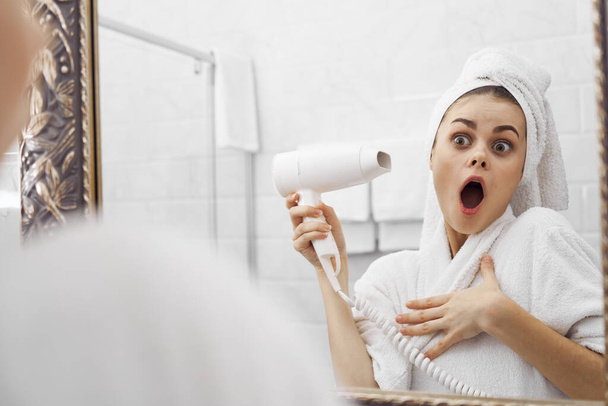 meglepett nő a fürdőszobában hajszárítóval a tükör előtt - Fotó, kép