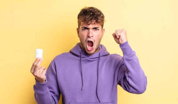 young handsome man shouting aggressively with an angry expression. pills bottle concept - Foto, afbeelding