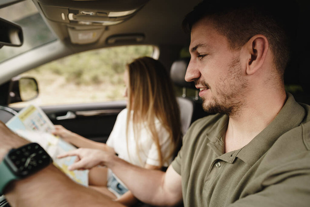 Young loving couple on a road trip using map inside a car - Photo, image