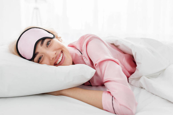 Sorrindo muito jovem mulher loira caucasiana em pijama rosa e máscara de sono desfrutando de bom dia - Foto, Imagem