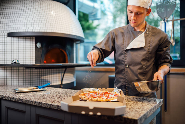 Chef sprinkles pizza in a box with spices. Catering kitchen work. - Fotoğraf, Görsel