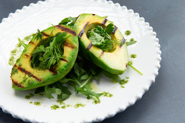 Жареный авокадо и зелень в тарелке на сером фоне. Селективный фокус. - Фото, изображение