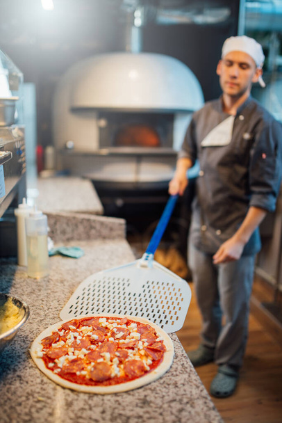 Chef takes pizza on the spatula. Catering kitchen work. - Zdjęcie, obraz