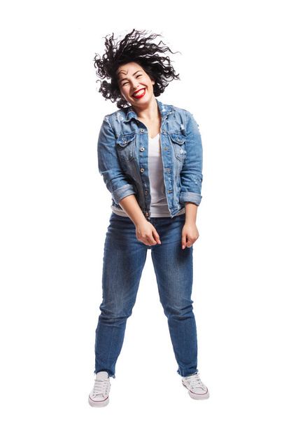 Young dancing plump girl. Beautiful curly brunette with red lips in jeans. Body positivity and freedom. Isolated on white background. Vertical. - Zdjęcie, obraz