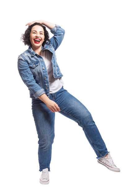Young dancing plump girl. Beautiful curly brunette with red lips in jeans. Body positivity and freedom. Isolated on white background. Vertical. - Foto, Imagem