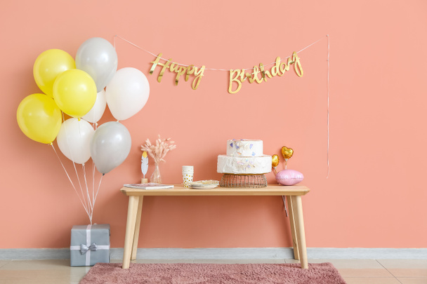 Table with birthday cake and balloons near color wall - Photo, image