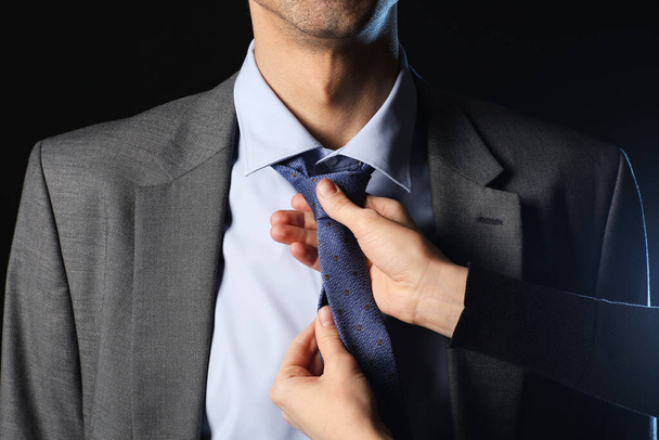 Женщина чинит мужской галстук на темном фоне - Фото, изображение