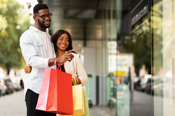 Retrato de pareja negra con bolsas de compras apuntando a la ventana - Foto, Imagen