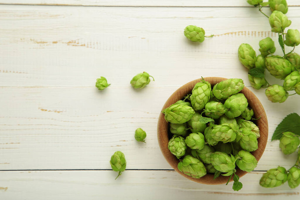 Wooden bowl with hops on white wooden background, space for text. Top view - 写真・画像