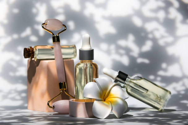 Butelki produktów kosmetycznych z narzędziem do masażu twarzy i kwiat na ciemnym tle - Zdjęcie, obraz
