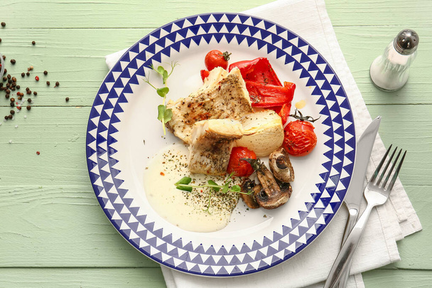 Plate with tasty baked cod fillet, vegetables and mushrooms on color wooden background - Photo, Image