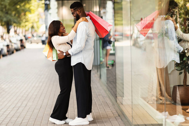 Χαρούμενο ζευγάρι Αφροαμερικανών αγκαλιάζει και κρατάει τσάντες για ψώνια - Φωτογραφία, εικόνα