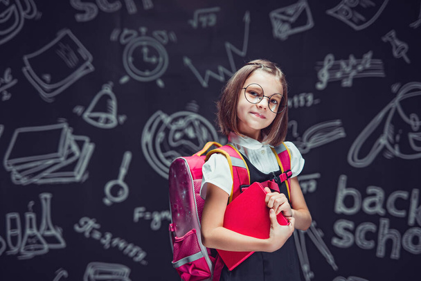 Cute schoolgirl in glasses preparing to go to school with backpack and book in hands Back to school  - Fotó, kép