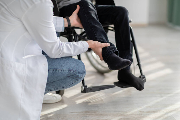 Γυναίκα γιατρός κάνει ασκήσεις φυσιοθεραπείας ή μασάζ σε ανάπηρο έφηβο αγόρι σε αναπηρική καρέκλα σε εσωτερικούς χώρους, closeup - Φωτογραφία, εικόνα