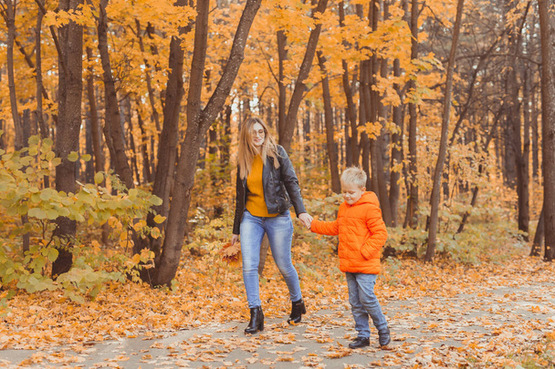 Moeder en zoon wandelen in het herfstpark en genieten van de prachtige herfstnatuur. Seizoen, eenouder- en kinderconcept. - Foto, afbeelding