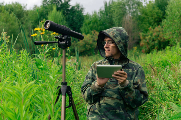 Der Ornitologe betrachtet oder notiert Informationen auf dem Tablet, während er im hohen Gras im Feuchtgebiet steht. - Foto, Bild