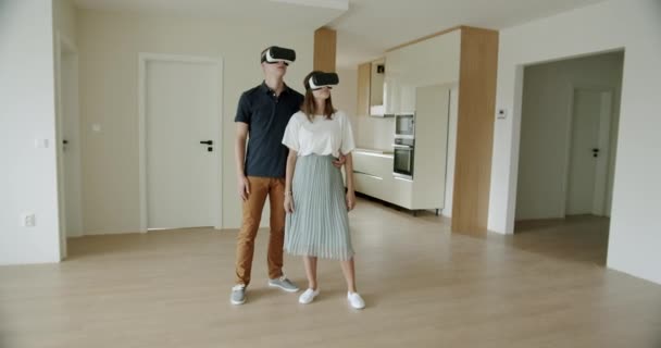 Mladý pár prohlíží nový byt s VR sluchátky. Poprvé kupující nosí sluchátka virtuální reality a dívají se na nový dům. Real-time, ruční záběr, široký záběr, 4K. - Záběry, video