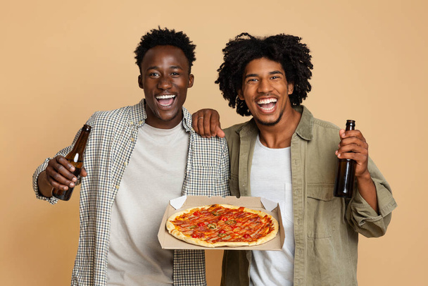 Fiesta para hombres. Dos felices amigos negros con cerveza y pizza en caja - Foto, imagen