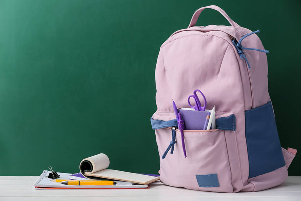 Стильный школьный рюкзак с канцелярскими принадлежностями на столе против доски - Фото, изображение