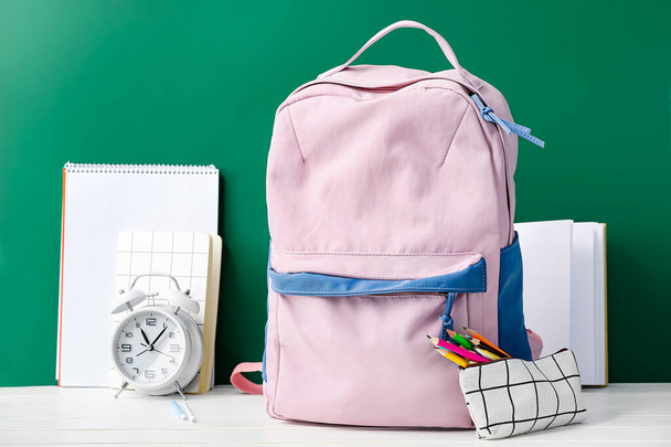 Stylish school backpack, stationery and alarm clock on table in classroom - Φωτογραφία, εικόνα