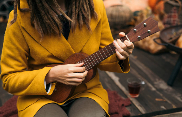 girl with dreadlocks closeup playing an acoustic instrument ukulele in autumn on the terrace. - 写真・画像