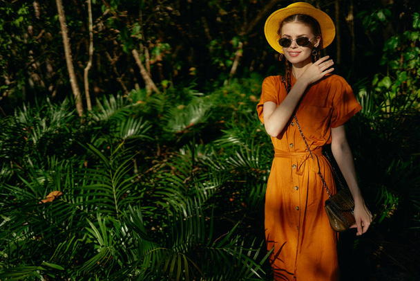 mujer en un vestido de naranja y sombrero camina en la naturaleza en el parque Selva exótica - Foto, imagen