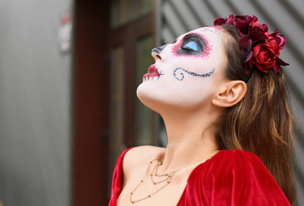Young woman with painted skull on her face outdoors. Celebration of Mexico's Day of the Dead (El Dia de Muertos) - Photo, Image