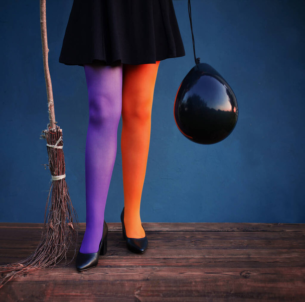 witch legs in multicolored tights with black balloon and broom on blue background - Foto, Bild