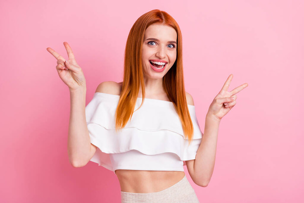 Portrait of attractive cheerful girlish red-haired girl showing double v-sign having fun isolated over pink pastel color background - 写真・画像
