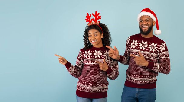 Weihnachtsgeschäft. Aufgeregtes afrikanisch-amerikanisches Paar zeigt beiseite auf leeren Raum für Ihre Werbung, blauer Hintergrund - Foto, Bild