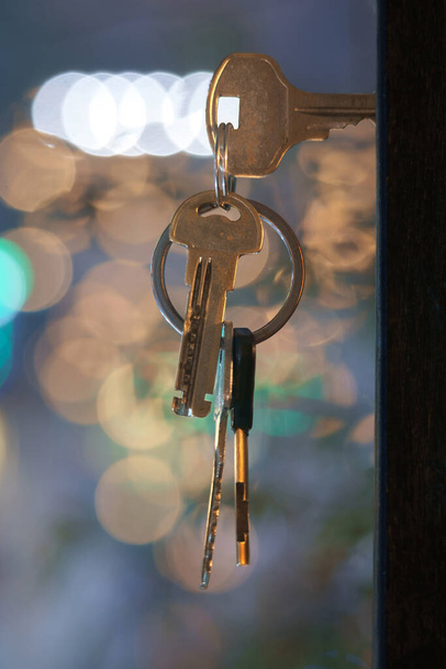 Ключі з домашніми клавішами у дверній щілині з розмитим фоном нічного освітлення, вибірковий фокус
 - Фото, зображення
