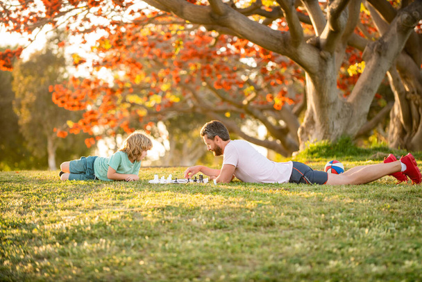 šťastná rodina tatínek a syn dítě hrát šachy na zelené trávě v parku venkovní, spolužití - Fotografie, Obrázek