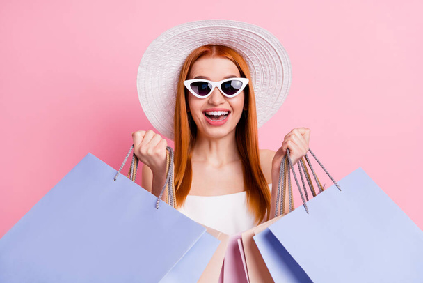 Fénykép vidám boldog szép fiatal nő fogja a kezét bevásárló táskák mosoly elszigetelt rózsaszín színű háttér - Fotó, kép