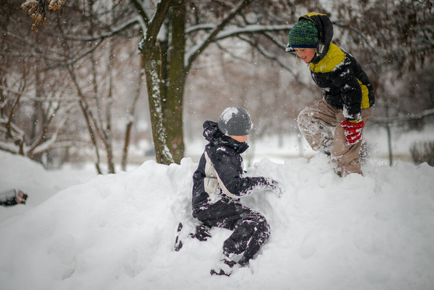 Dos chicos juegan en la pila de nieve después de fuertes nevadas en la ciudad. Los niños en un paseo por el parque en invierno. Estilo de vida saludable activo. - Foto, Imagen