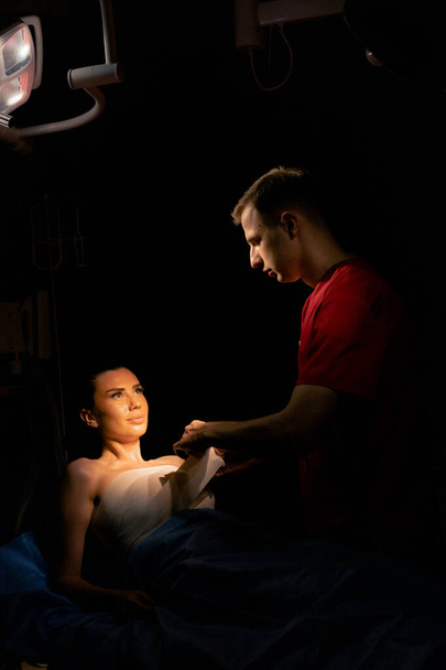 Chirurg s pacientkou na operačním sále před zvětšení prsou pro dívku. Lékař obtočí kolem pacientova hrudníku po zvětšení prsou. - Fotografie, Obrázek