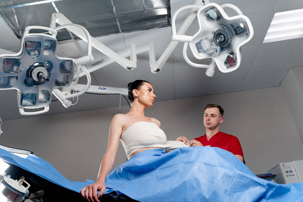 Chirurg mit Patientin im Operationssaal vor Brustvergrößerung für Mädchen. Arzt wickelt Patientin nach Brustvergrößerung um Brust. - Foto, Bild