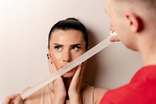 Модель с приклеенным ртом. Мужчина прикрывает женский рот лентой. Хватит болтать. - Фото, изображение