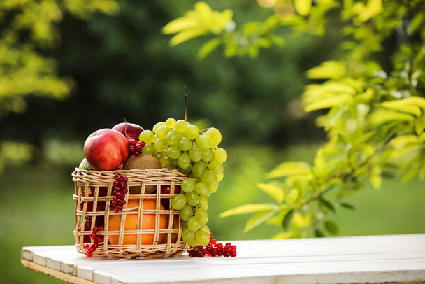 Cesta de mimbre con frutas frescas en la mesa al aire libre - Foto, imagen