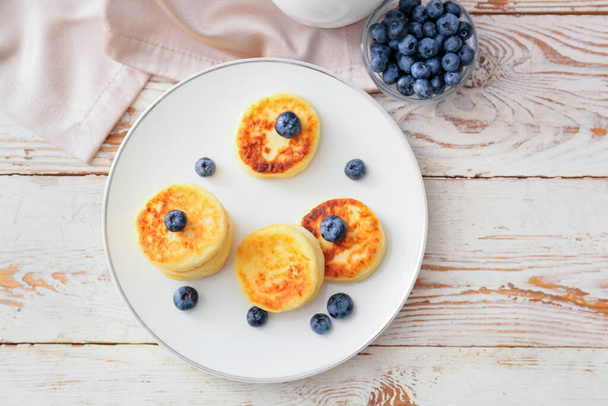 Plate with cottage cheese pancakes and blueberries on light wooden background - Foto, imagen