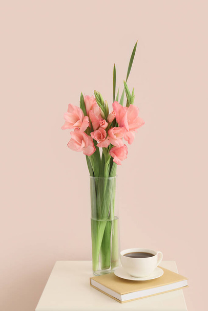 Ваза с цветами гладиолуса, чашка кофе и книга на столе в номере - Фото, изображение