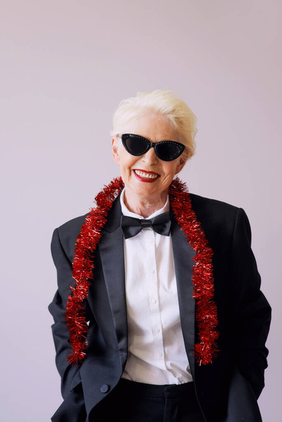Krásná stylová starší žena ve slunečních brýlích a smokingu slaví nový rok. Zábava, párty, styl, koncepce oslav - Fotografie, Obrázek