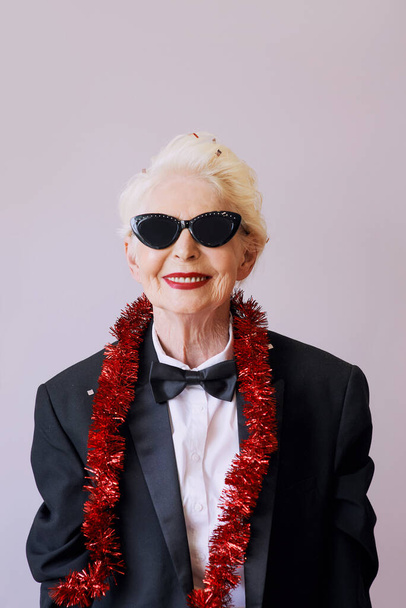 Gyönyörű, elegáns, idősebb nő napszemüvegben és szmokingban ünnepli az új évet. Szórakozás, buli, stílus, ünnep koncepció - Fotó, kép