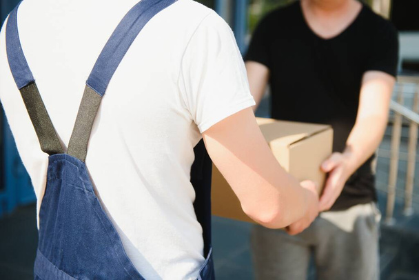 Delivery man service with boxes in hands standing in front of Customer's house doors - 写真・画像