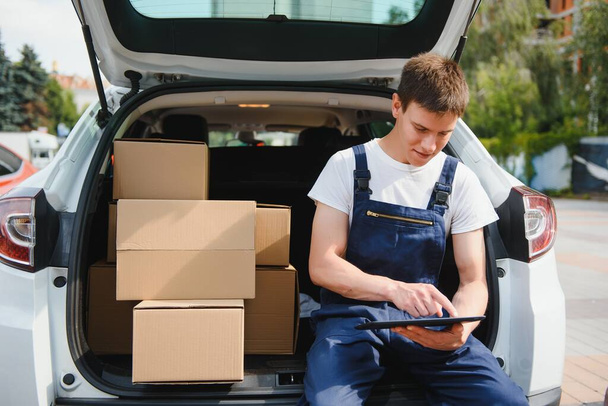 Young male courier with parcels near delivery service car - Fotó, kép